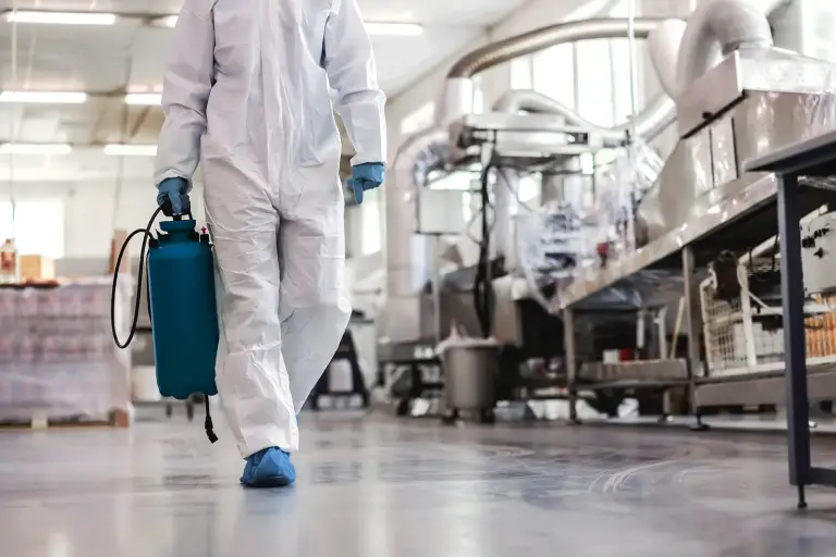 Protective suit worker carrying sprayer in factory