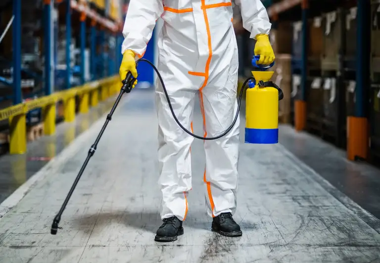 Worker in protective suit spraying disinfectant